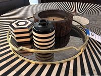 Overview of tray with vessels, wooden candle holder, and wooden box on a round table with striped pattern.