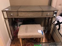 Front view of the wood vanity desk with mirrored legs, three drawers, and matching upholstered stool showing some surface wear.