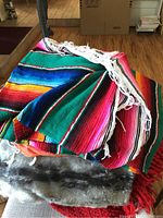 Colorful striped Mexican style woven throw with white fringes and fuzzy gray throw beneath, displayed on a surface