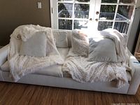 Front view of white West Elm sofa with matching pillows and plush throw blanket in living room by French doors.