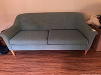 Front view of the West Elm sofa showing two removable seat cushions, fabric upholstery, button tufting on backrest, and wooden legs.