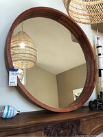 View of the large round wall mirror with segmented wood frame reflecting a woven lamp and interior features.