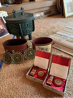 Lot contents on carpet including ice bucket, two ceramic containers, three small round metal wall art pieces, two boxed good luck items