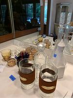 Photo of two clear glass decanters, one with stopper, and assorted glassware including mugs with metal holders and small cups