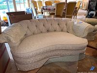 Breuners curved sofa in light patterned fabric, tufted back, and cushioned, curved seat shown angled from the side.