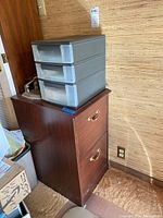 Wooden file cabinet with plastic storage bin on top, placed against wall