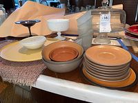 Wide shot of the lot showing all included items arranged on a table, including the glass cake plate with dome, metal cake stand, ceramic dishes, saucers, bowls, yellow platter, and frosted glass votives.