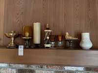 Front view showing all 8 candleholders including brass metal bowl, amber glass cups, pillar candle, lantern, votive holders, decorative bird on pedestal, and white ceramic vase candleholder.