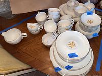 Photo of teacups, cream and sugar bowl, some plates, and bowls with gold wheat motif, white background