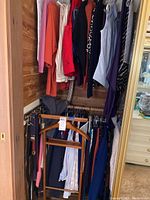 Photo showing various ladies clothes hanging in closet including sweaters, skirts, jackets, belts and a hanger.