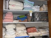 View of shelves with stacked towels, linens, mattress pads, and comforters in plastic.