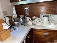 Cuisinart stand mixer, Osterizer blender, Oster juicer, Hamilton Beach mixer, metal utensils, and VTech baby monitor on kitchen counter