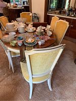 Photo showing oval wooden dining table set with chairs around it, also holding dishware not included in sale.