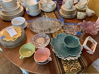 Overview of all plates, cups, serving dishes, ashtrays placed on wooden table, showing variety of items.
