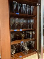 Four wooden shelves filled with various glassware including martini, wine, and cocktail glasses.