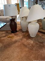 Three lamps together on carpet, includes one brown lamp from Macy's and two white ribbed ceramic lamps, all with shades.