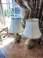 Two lamps with white fabric shades and gold-tone round bases, positioned near a window with natural light.