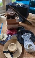 Overview of the lot showing a large black suitcase, several hats including straw and crocheted, multiple small bags and totes, and a plastic bag with packing material.
