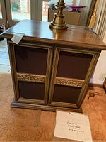Two wooden McIntosh cabinet speakers side by side with fabric grille covers, carved wood trim, floor lamp on top, and note on floor indicating stereo cable inside box.