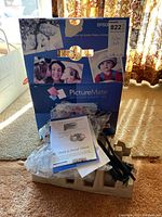 Closed box of Epson PictureMate personal photo lab printer showing front cover with images of printed photos and product branding.