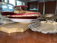 Platters, cutting board, wooden utensils and silver-tone scalloped edge serving tray shown stacked on a surface