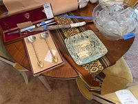 Overview of a round wooden table holding a clear glass punch bowl with matching small glass cups, a green-speckled square ceramic plate, and two gold-tone serving forks.