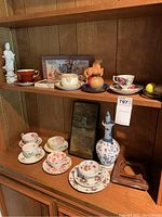 Wide shot capturing multiple tea cups and saucers, coasters, blue and white decanter, and other shelf decorative items