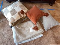 Three throw pillows and one beige blanket arranged on carpet in front of wooden furniture