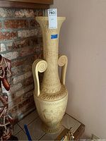 Full view of tall neoclassical decorative vase with spiral handles, positioned near a brick wall.