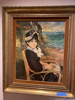 Photo of framed wall art print showing a woman in a bonnet seated by the seaside, set in an ornate gold frame.