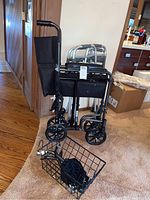 Photo of folded wheelchair with black fabric, wheels, and a detachable basket on the floor in front