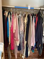 Photo showing a rack of women's clothing including tops, skirts, and jackets in various colors, some covered in plastic.