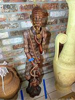 Full view of tall wooden fisherman statue standing against brick wall.
