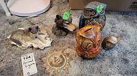 Photo of all animal figurines including two wolf figurines, two pottery owls (one piggy bank), and pottery sun decoration on carpet.