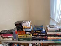 Books arranged on a table including various authors such as Ken Follett, Tom Clancy, John Grisham, Danielle Steel, Judith Krantz, and others.