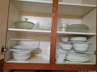 Cabinet with shelves containing white Corelle dinner plates, bowls, and several glass bowls