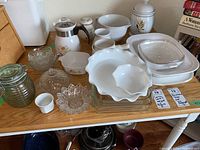 Overview of the collection on a wooden table showing multiple glass dishes, Corning Ware coffee pot, and bowls.