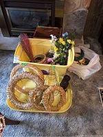 Yellow plastic bins filled with floral crafting supplies including artificial flowers, straw wreath frames, floral wire cone form, and ribbons.