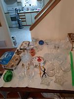 Overview of lot showing glass bowls, wine glasses, ashtrays, figurines, China plates, and kitchen background.