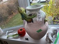 Wide view of large pink ceramic vase with green iguana climbing side, ceramic pumpkin, leaf-shaped spoon holders, tiny black figurines, and white ceramic polar bear on window sill.