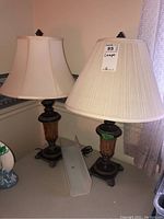 Pair of metal base table lamps with fabric shades, one with smooth cream shade and one with pleated off-white shade, standing side by side
