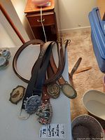 Set of 5 leather belts laid out showing varied belt buckles including Harley Davidson, British Bulldog Spirit, Algonquin Park Ranger, and other designs.