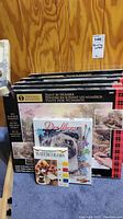 Photo showing multiple boxed paint by number kits stacked, front visible with Thomas Kinkade labeled box on top