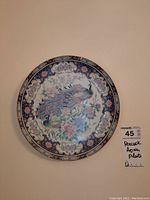 Photo of a hanging decorative bone china plate with a peacock and floral design on dark blue background with gold accents