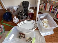 Wide view of assorted kitchenware including roasting pan, measuring cups, cups, saucers, serving dishes, muffin and baking tins, and pizza pans.