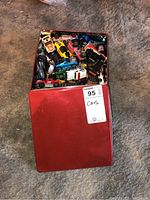 Red tin box showing multiple toy cars inside, partially covered lid, view of varied toy cars.