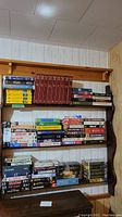Photo showing multiple shelves with numerous VHS and DVD cases, clearly showing the collection size and arrangement on wall-mounted wooden shelves.