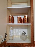Seven vintage glasses with red and gold ornate design on top shelf of cabinet