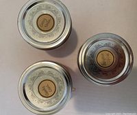 Top view of three metal lid mason jar candle tops showing scent labels: Candy Cane, Pumpkin Spice, Lacey Linen.