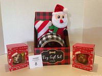 Front view of the dog gift set showing the bowl and two Christmas plush toys in a red and black plaid box flanked by two boxed dog Christmas ornaments featuring a Yorkie and Yellow Lab.